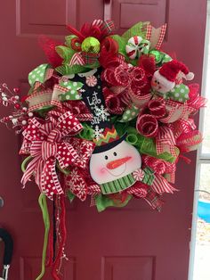 a christmas wreath hanging on the front door decorated with red and green ribbons, snowman ornament