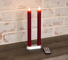 two red candles sitting on top of a table next to a remote control and brick wall