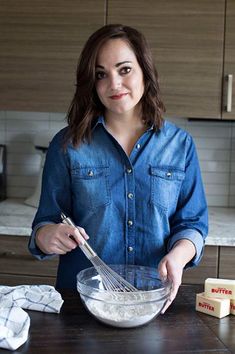 a woman standing in front of a kitchen counter holding a whisk and mixing bowl