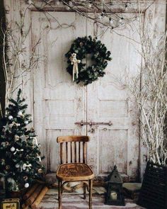 a chair sitting next to a christmas tree in front of a white door with a wreath on it