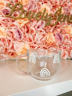 a glass cup sitting on top of a table next to a pink flower covered wall