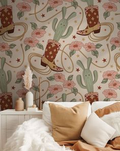 a white bed topped with pillows next to a wallpaper covered in cactus and stars