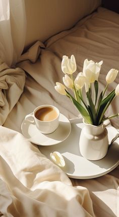 a cup of coffee and some white tulips on a tray in the bed