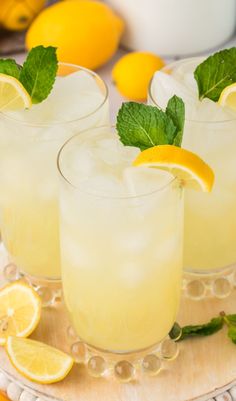 two glasses filled with lemonade and mint garnish on a plate next to sliced lemons