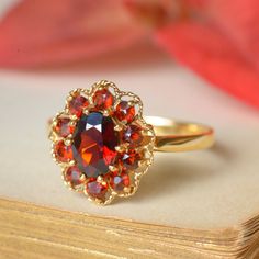 A delightful vintage English, halo-style dress ring, cluster-set with natural garnet. Measuring 7x5mm (0.75ct), the central oval garnet is surrounded by a halo of 10 round-cut garnets totalling approximately 0.30ct. Crafted from 9ct yellow gold, the face of the ring is encircled by a fine twisted wire-work frame, completing the impression of a lacey-edged flower head. Sweet, colourful and so very cheerful! The perfect accessory for a vintage spring outfit. This ring is a size N (AU/UK) or 6 3/4 Vintage Garnet Cluster Ring As Gift, Heirloom Oval Garnet Cluster Ring, Vintage Cluster Ring With Halo Design, Vintage Garnet Cluster Ring With Gemstone, Vintage Cluster Ring Suitable For Gifts, Antique Oval Cluster Ring As Gift, Vintage Garnet Cluster Ring For Anniversary, Antique Oval Cluster Ring For Gift, Vintage Wedding Ruby Cluster Ring