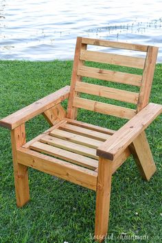 a wooden chair sitting on top of a lush green field next to a body of water