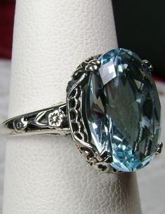 Simulated Aquamarine Ring Edward Design#70 Custom Made Here we have an Edwardian reproduction ring in sterling silver filigree with a perfect Simulated/Man-made blue aquamarine gemstone solitaire. This full cut oval gem is 14mm in length and 10mm in width (slightly smaller gemstone also available upon request). This ring also sits 7mm off the finger. The inside of the band is marked 925 for solid sterling. Notice the beautiful leaf design of the silver filigree setting and etched band. This is a Exquisite Sterling Silver Topaz Ring With Center Stone, Exquisite Silver Topaz Wedding Ring, Exquisite Silver Topaz Ring For Wedding, Classic Aquamarine Gemstone Jewelry, Exquisite Sterling Silver Topaz Ring, Exquisite Silver Topaz Ring With Accent Stones, Vintage Sterling Silver Topaz Ring With Accent Stones, Vintage Sterling Silver Topaz Gemstone Ring, Oval Gemstone Filigree Ring For Formal Events