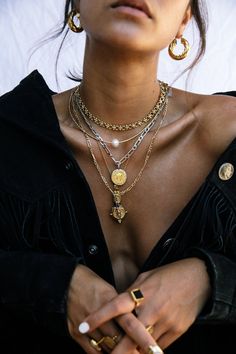 a close up of a person wearing gold jewelry and holding her hands in their pockets