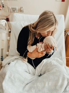 a woman holding a baby in her arms while sitting on top of a hospital bed