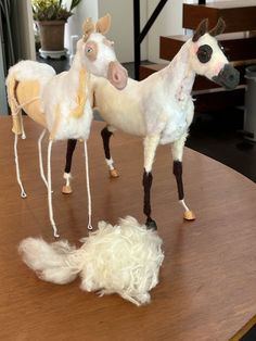 two fake horses standing on top of a wooden table next to a pile of wool