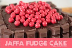 there is a chocolate cake with red candies on top and the words jaffa fudge cake below it