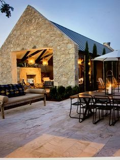 an outdoor dining area with patio furniture and stone building in the background at night time