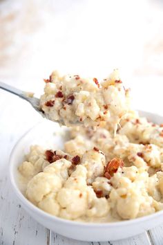 a spoonful of mashed potatoes with bacon on top is being held up in a bowl