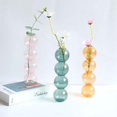 three vases with flowers in them sitting on top of a white table next to a book