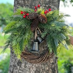 a christmas wreath hanging from the side of a tree next to a bell with red berries on it