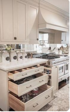 an open drawer in the middle of a kitchen with white cabinets and drawers on both sides