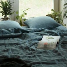 a book is laying on top of a bed with blue sheets and pillows in front of a window