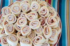 a plate filled with rolled up sandwiches on top of a striped table cloth next to a cup of coffee