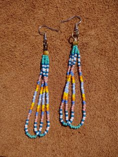 two pairs of beaded earrings are hanging from hooks on a brown carpeted surface