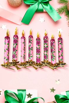 a bunch of candles that are next to some christmas decorations on a pink background with green ribbons