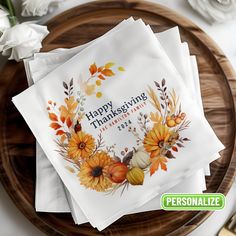 thanksgiving napkins with flowers and leaves are on a wooden plate next to white roses