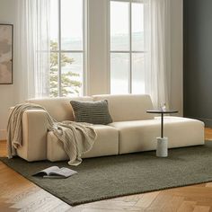 a white couch sitting on top of a wooden floor next to a window covered in curtains