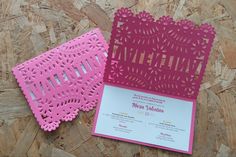 two pink and white wedding cards with laser cut designs on them, sitting on wood planks