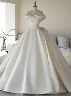 a white wedding dress on display in front of a couch with pillows and vases