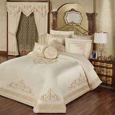 a bed with white comforter and pillows in a room next to a dresser, mirror and lamp