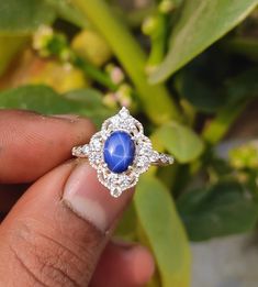 a close up of a person's hand holding a ring with a blue stone