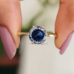 a woman's hand holding an engagement ring with a blue diamond in the center