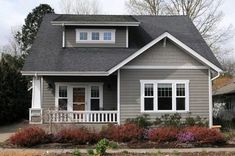 a gray house with white trim and two windows on the second floor is surrounded by shrubs and flowers