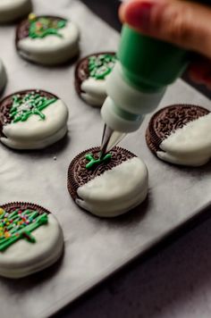 someone is decorating cookies with white icing and green decorations on the cookie sheet