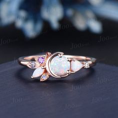 an opal and diamond ring on top of a black surface with flowers in the background