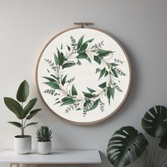 a white wall with some plants on it and a round frame hanging above the table