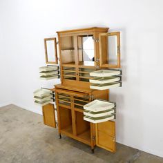 a wooden cabinet with many drawers and plates on the top, in front of a white wall