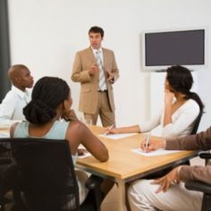 a group of people sitting around a table in front of a man giving a presentation