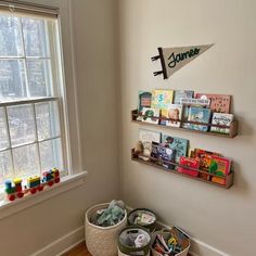 the corner of a room with two baskets and books on the wall next to a window