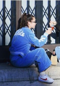 two women sitting on the steps drinking coffee and talking to each other while wearing matching outfits