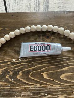 a white beaded necklace and tube of e 6000 glue on a wooden table