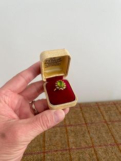 a person is holding an open ring box with a small green flower in it's center