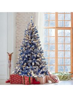 a blue and white christmas tree in front of a window with presents on the floor