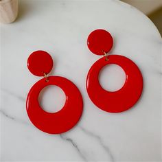 Stylish Red Dangle Hoops with a Modern Twist. Red hoop earrings in a retro style are always in vogue, having remained popular across several decades, from the 50's, 60's, 70's, 80's, and beyond. Handmade with care, these earrings are not only trendy but also enjoyable and fun to wear. Treat yourself or surprise a friend with a gift of these vibrant, medium-sized hoops made from polymer clay and coated with resin on both sides. Featuring an open circular orange hoop at the bottom connected to mat Red Clip-on Earrings For Party, Trendy Red Circular Jewelry, Retro Red Dangle Earrings, Red Pierced Hoop Earrings For Party, Red Pierced Hoop Earrings, Modern Red Round Earrings, Retro Hoop Earrings For Parties, Trendy Red Hoop Earrings For Party, Vintage Red Drop Clip-on Earrings