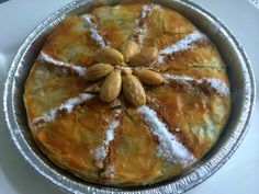 a pie with almonds and powdered sugar on top sits in a tin pan