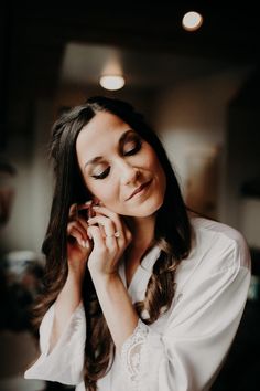 a woman with long hair wearing a white shirt and holding her hands to her face