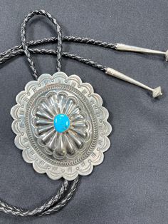 "This is a large silver scalloped concho bolo tie with a bright blue turquoise stone in the center. Silver tips on the ends of the leather measure 2.35\". Great gift or accessory to wear for an anniversary, birthday or an amazing wedding suit tie, everyday, with a suit or dress as a necklace.  68 grams for the entire piece Tie: 23\" long Scalloped Concho: 4\" long x 3.5\" wide Silver Tips: 2.35\" If you have questions about this item etc please ask before you purchase. Sold as is, no returns on vintage items. I do not polish any jewelry - I sell it as it is received, if pieces are tarnished you can polish them to a high shine but I leave that up to the customer. Free domestic shipping.  Thanks for looking. Julie B. PLEASE read my shop policies http://www.etsy.com/shop_policy.php?user_id=51 Artisan Silver Bolo Tie With Concho, Silver Western Bolo Tie, Vintage Silver Bolo Ties With Concho, Sterling Silver Bolo Tie, Handmade Vintage Turquoise Bolo Ties, Bolo Tie, Western Art, Tie Accessories, Suit And Tie