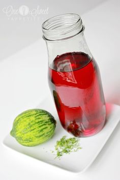 a glass jar filled with liquid next to a melon on a white plate,