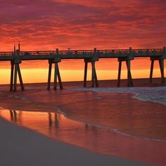 a long pier stretches out into the ocean as the sun sets over the water and reflects in the wet sand