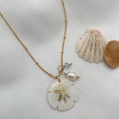 Legend has it that finding a sand dollar during a beach stroll is considered a lucky omen. So take a little bit of the beach and good luck with you wherever you go with our gorgeous Sand Dollar Charm Necklace. Features our most loved satellite chain, freshwater pearl, and blue zircon accents. Freshwater Baroque Pearl size: 6 to 8mm Blue Zircon roundel gemstone 4mm 14kt gold fill or sterling silver round beads 2mm 14kt gold fill or sterling silver satellite chain Real sand dollars are preserved a Beach Sand Necklace, Sand Dollar Jewelry, Dainty Starfish Necklace For Beach, White Ocean-inspired Charm Necklace For Gift, Ocean-inspired White Charm Necklace As Gift, Ocean-inspired White Charm Necklace Gift, Dainty Shell Charm Necklace For Beach, White Delicate Chain Necklace For Beach, Ocean-inspired Strand Charm Necklaces As Gift