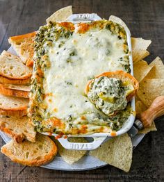 a white plate topped with cheese and spinach dip surrounded by tortilla chips